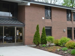 Front entrance of two storey brown brick building with flower beds lining the walkway